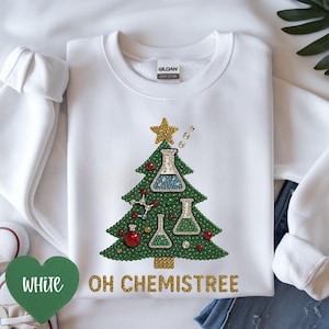 Puede incluir: Sudadera blanca con un diseño de árbol de Navidad verde hecho de purpurina y equipo de laboratorio. El árbol está adornado con una estrella dorada, adornos rojos y el texto "OH CHEMISTREE".