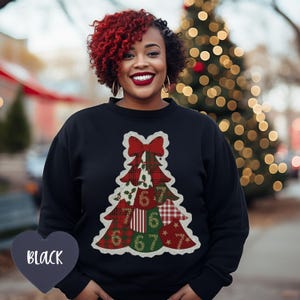 May include: Black crew neck sweatshirt featuring a Christmas tree design. The tree is composed of various plaid and patterned fabrics, with a red bow at the top and the numbers 6 and 7 throughout. The sweatshirt is a holiday-themed apparel item.