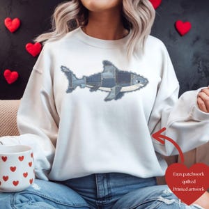 Op de afbeelding: Een witte sweatshirt met een faux patchwork haai ontwerp. De haai is gemaakt van denim patches, waardoor het een textuur krijgt. De bedrukte artwork staat op de voorkant van de sweatshirt, wat een casual look geeft.