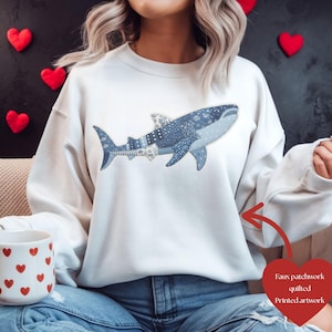 Op de afbeelding: Wit sweatshirt met een blauwe walvishaai-design. De walvishaai heeft een blauw en wit patchwork patroon. Het sweatshirt heeft een ronde hals.