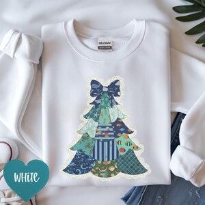 May include: White sweatshirt with a patchwork Christmas tree design. The tree features sea-themed patterns like whales, fish, and seashells. The word "WHITE" is displayed on a teal heart-shaped tag. The sweatshirt is made of cotton.