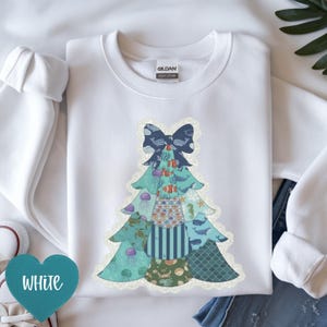 Op de afbeelding: Witte sweatshirt met een patchwork kerstboomontwerp. De boom is versierd met zeedierenpatronen, waaronder walvissen, kwallen en zeepaardjes, en is afgewerkt met een marineblauwe strik. Het woord "WHITE" wordt weergegeven op een turquoise hartvormig label.