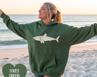Könnte beinhalten: Waldgrüner Kapuzenpullover mit weißer Hai-Grafik. Der Hoodie hat eine Kängurutasche und eine Kapuze mit Kordelzug. Der Text "FOREST GREEN" befindet sich in einer herzförmigen Grafik. Die Person ist am Strand.