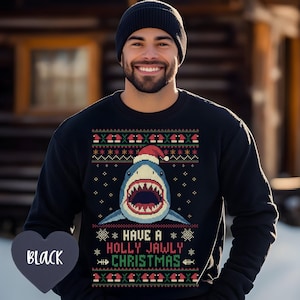 May include: Black crew neck sweatshirt with a shark wearing a Santa hat. The shark has an open mouth with visible teeth. The text "Have a Holly Jawly Christmas" is below the shark, with snowflake and fishbone accents.