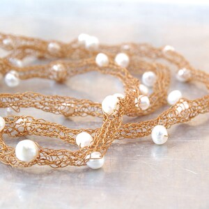 Könnte beinhalten: Eine goldene Drahtkette mit weißen Perlen. Die Kette ist gehäkelt und hat einen zarten, femininen Look.