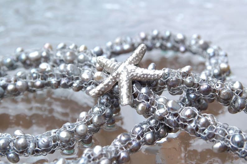 K&ouml;nnte beinhalten: Eine silberne Kette mit einem silbernen Seestern-Anh&auml;nger und grauen Perlen. Die Kette ist aus Draht und Perlen gefertigt.