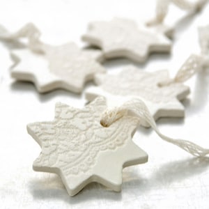 May include: A string of white ceramic star ornaments with a lace design, connected by white ribbon.