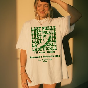 May include: White t-shirt with a green pickle graphic and the text "LAST PICKLE" repeated multiple times. The shirt also includes the text "I'll ever tickle" and "Amanda's Bachelorette Los Angeles, CA 2026".