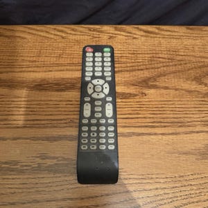 May include: A black rectangular remote control featuring a numeric keypad, a central directional navigation pad, and numerous function buttons labeled with white text. The device includes a red power button and a green button at the top.