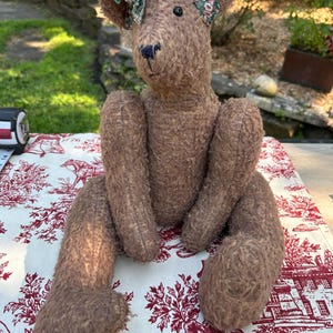 584 Vintage jointed teddy bear, featuring a shaggy brown, plush texture and dark green floral bow