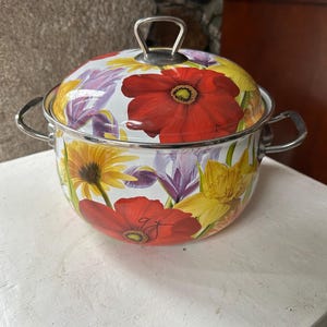 May include: A white enamel cooking pot with a lid, adorned with a vibrant floral pattern featuring red poppies, yellow sunflowers, and purple irises. The pot has silver handles and a matching lid handle.