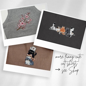 K&ouml;nnte beinhalten: Drei Shirts mit gestickten Katzenmotiven: ein graues Shirt mit Kirschbl&uuml;tenzweig und kleinen Katzen, ein schwarzes Shirt mit f&uuml;nf Katzen auf einer Linie und ein braunes Shirt mit einem vertikalen Stapel aus vier Katzen. Text: more funny cute cat shirts see Shop.