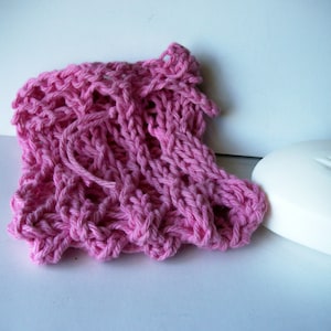 May include: A pink knitted washcloth with a textured pattern. The washcloth is made of soft yarn and is perfect for gentle exfoliation.