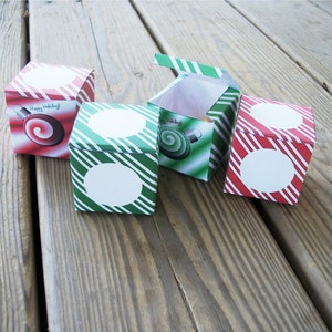 May include: Four small, red and green striped boxes with white circles. The boxes are decorated with images of Christmas baubles. One box has the text "Happy Holidays!" on it.