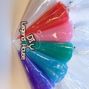May include: A collection of colorful, cone-shaped DIY slime kits in clear plastic bags. The slimes are in shades of white, red, pink, green, blue, and purple, with glitter accents. The bags are tied with gold twist ties. The text "DIY House Legend" is visible.