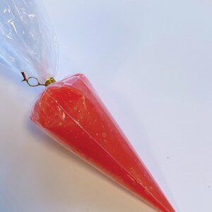 May include: A clear plastic piping bag filled with bright red icing. The icing has small white specks throughout. The bag is sealed at the top with a gold-colored twist tie and a clear plastic bag.