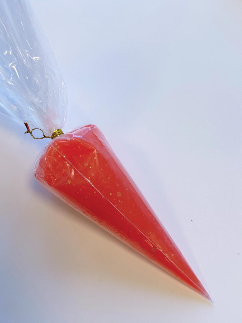 May include: A clear plastic piping bag filled with bright red icing. The icing has small white specks throughout. The bag is sealed at the top with a gold-colored twist tie and a clear plastic bag.