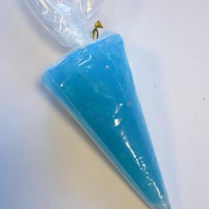 May include: A clear plastic piping bag filled with light blue frosting. The frosting has a slightly glittery appearance. The top of the bag is twisted and secured with a gold-colored twist tie. The bag is on a white surface.