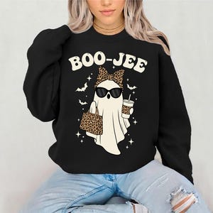 May include: Black sweatshirt with a graphic of a ghost wearing sunglasses, a leopard print bow, and carrying a leopard print bag and a coffee cup. The text "BOO-JEE" is above the ghost. Bats and stars surround the ghost.
