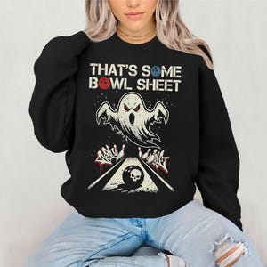 May include: Black sweatshirt with a bowling-themed graphic. The design features a ghost, bowling pins, and a bowling ball with a skull. The text "THAT'S SOME BOWL SHEET" is printed above the graphic. The sweatshirt is worn by a person.