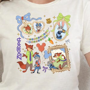 Op de afbeelding: Cr&egrave;mekleurig T-shirt met kleurrijke cartoonillustraties van personages uit de film "Zootopia". Het ontwerp bevat ingelijste portretten, een wortel en het woord "Zootopia" in een verticale lettertype. Het shirt heeft korte mouwen.