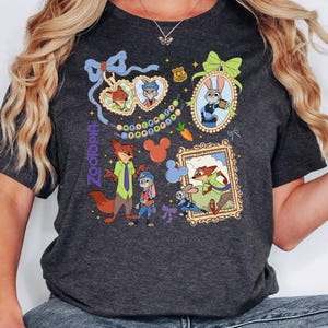 Op de afbeelding: Donkergrijs T-shirt met kleurrijke illustraties van personages uit de animatiefilm Zootopia. Het ontwerp bevat ingelijste portretten, karakterkoppels en het logo van de film. Het shirt heeft een ronde hals en korte mouwen.