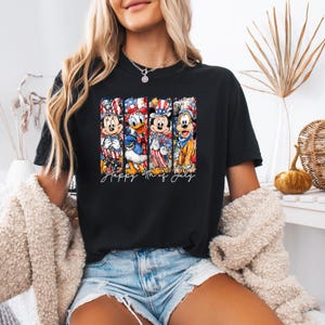 Pode incluir: Camiseta preta com um design de personagens da Disney em trajes patri&oacute;ticos, incluindo Mickey Mouse e Pato Donald. O texto "Happy 4th of July" est&aacute; escrito em it&aacute;lico. O design utiliza as cores vermelho, branco e azul.
