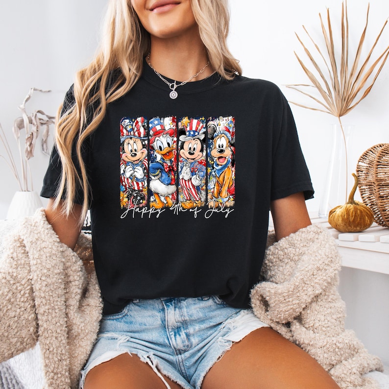 Pode incluir: Camiseta preta com um design de personagens da Disney em trajes patri&oacute;ticos, incluindo Mickey Mouse e Pato Donald. O texto "Happy 4th of July" est&aacute; escrito em it&aacute;lico. O design utiliza as cores vermelho, branco e azul.