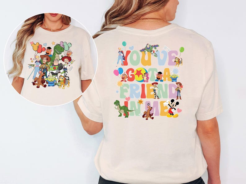 May include: Cream-coloured t-shirt with a colourful graphic of Toy Story characters and the phrase "You've Got a Friend in Me." The design includes Woody, Buzz Lightyear, Rex, and other characters from the animated film.