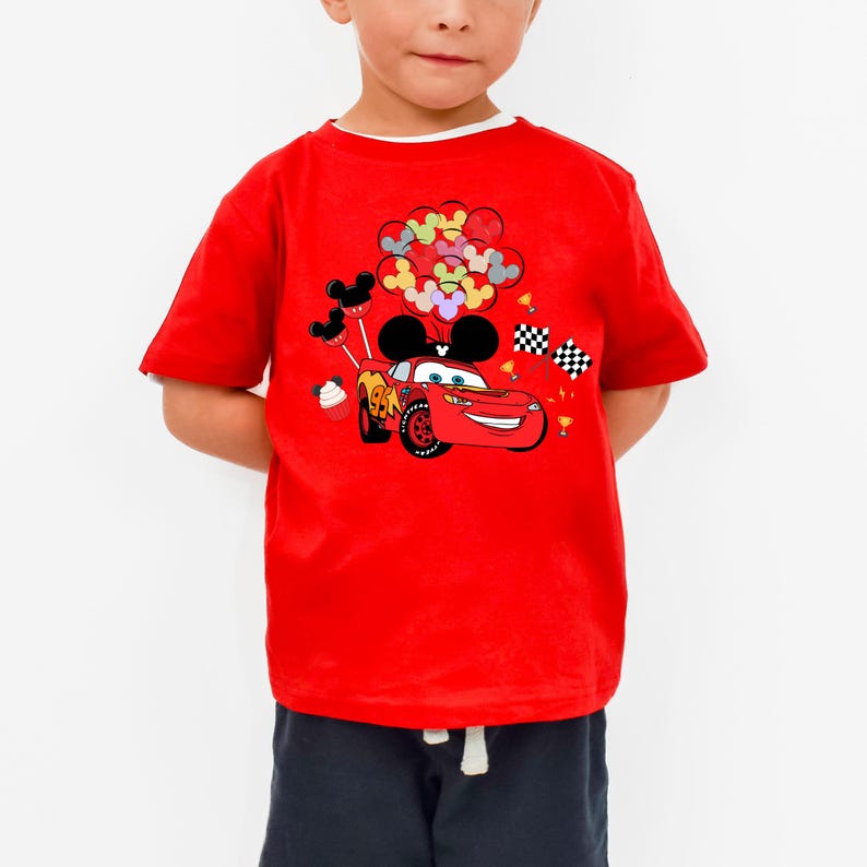 K&ouml;nnte beinhalten: Rotes T-Shirt mit einer Grafik von Lightning McQueen aus dem Film Cars, mit Mickey Mouse Ohren und bunten Luftballons. Das Design umfasst karierte Flaggen und einen Cupcake. Das Shirt hat einen wei&szlig;en Kragen.
