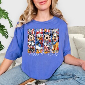 Pode incluir: Camiseta azul com um desenho do Mickey, Pato Donald e Pateta em trajes patri&oacute;ticos. As palavras "Happy 4th of July" est&atilde;o escritas abaixo dos personagens. A camiseta &eacute; de estilo casual e confort&aacute;vel.
