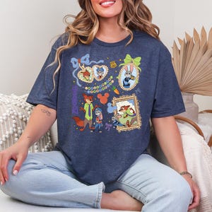 Op de afbeelding: Marineblauw T-shirt met stripfiguren uit Zootopia. Het ontwerp bevat ingelijste portretten van de personages, wortels en decoratieve elementen. Het T-shirt is gemaakt van een zacht materiaal.