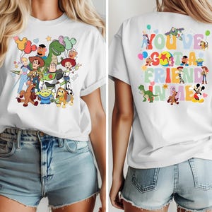 May include: White t-shirt with a vibrant graphic of Toy Story characters, such as Woody, Buzz Lightyear, and Rex. The back of the shirt has the text "You've Got a Friend in Me" and more character illustrations. A cheerful and playful design.