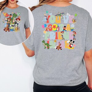 May include: A grey t-shirt with cartoon characters on the front and back. The front has a group of characters, and the back says "You've Got a Friend in Me" with more characters in a colourful design.