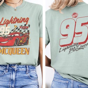 以下が含まれることがあります： ライトニング・マックィーンのグラフィックがプリントされた、薄い緑色のTシャツ。前面には95番、赤い車、そして「Lightning McQueen」の文字が描かれています。背面には大きな95番と「Lightning McQueen」の文字がプリントされています。