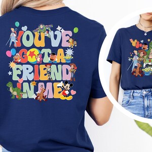 May include: A navy blue t-shirt with a vibrant graphic. The design features the phrase "You've Got A Friend In Me" and cartoon characters such as Buzz Lightyear and Mickey Mouse. The shirt is a classic crew neck.