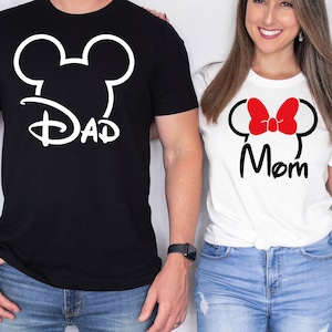 May include: Black t-shirt with a white Mickey Mouse head design and the word "Dad". White t-shirt with a red bow, black Mickey Mouse head design, and the word "Mom". Both shirts are short-sleeved.