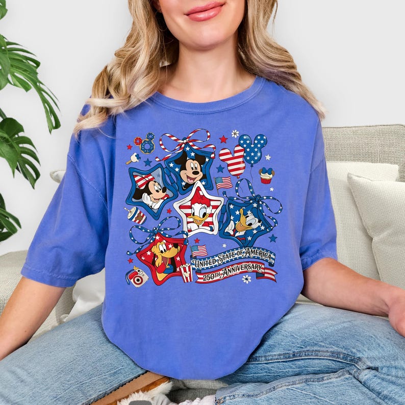 May include: A blue t-shirt with cartoon characters Mickey Mouse, Donald Duck, and others, framed by stars and patriotic ribbons. The shirt has the text "UNITED STATES OF AMERICA 250TH ANNIVERSARY".