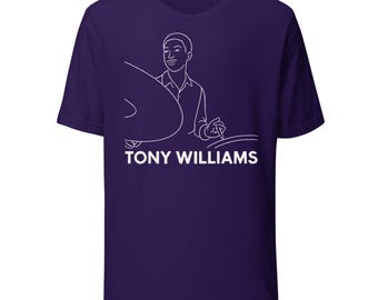 May include: A purple t-shirt featuring a white line drawing of Tony Williams, a jazz drummer, with a cymbal and drumsticks. The text "TONY WILLIAMS" is printed in white below the illustration. The shirt is made of a soft material.
