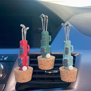 May include: Three golf-themed car air fresheners. Each has a miniature golf bag in red, green, and blue, with silver golf clubs and a white golf ball. They are mounted on cork bases.
