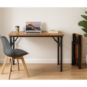 May include: A brown and black folding desk with a laptop, coffee cup, and a gray chair. The desk is made of wood and metal. A folded desk is leaning against the wall. A potted plant is in the background.