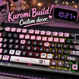 May include: Custom keyboard with black and pink keycaps, featuring the text "Kuromi Build! Custom decor." The keyboard has a silver frame and is decorated with Kuromi character designs. The time on the digital clock is 10:27.
