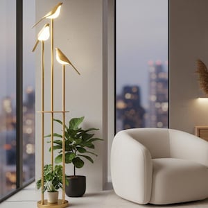 May include: A modern living room featuring a gold bird-shaped floor lamp with three lights. A white armchair sits near a large window overlooking a cityscape. Decorative plants and a wooden cabinet complete the scene.