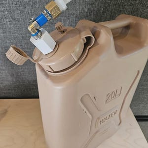 May include: A tan 20-liter water container with a white and blue adapter and a brass fitting. The container has a handle and the word "WATER" is embossed on the side. The cap is open.