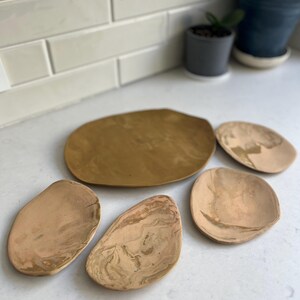 May include: A set of three ceramic mugs with a speckled, matte finish. The mugs are in shades of cream, light gray, and dark gray. Each mug has a simple, minimalist design, perfect for coffee or tea.