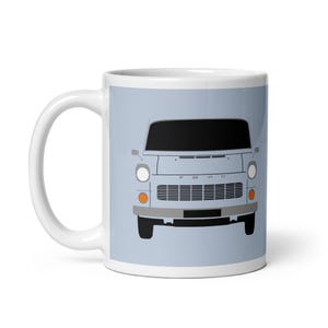 Może przedstawiać: Biały ceramiczny kubek z jasnoniebieskim tłem, przedstawiający grafikę klasycznego vana Forda. Van jest jasnoniebieski z czarnymi oknami, srebrnym zderzakiem i napisem "FORD" z przodu. Kubek ma biały uchwyt.