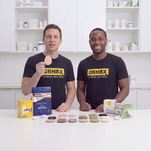 Puede incluir: Dos personas con camisetas negras con el logotipo amarillo de OHMRX Clinical Wellness. Sobre la mesa hay varios parches adhesivos en tonos neutros, una caja de Libre 3 Plus, una bolsa azul de OHMRX Patch Plus Wipes y envases de Dexcom G7.