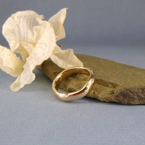 Op de afbeelding: Een eenvoudige gouden ring met een glad, afgerond oppervlak. De ring ligt op een stuk bruin gesteente.