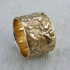 Könnte beinhalten: Ein breiter Goldring mit einer strukturierten Oberfläche. Der Ring hat ein raues, organisches Aussehen.