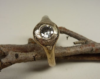 May include: A gold ring with a textured band and a single round clear gemstone set in the centre.